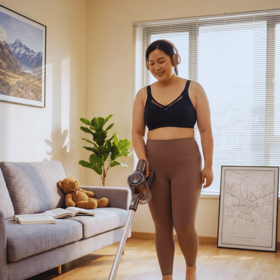 Plus size lady wearing headphones, vacuumning the floor with a stick vacuun